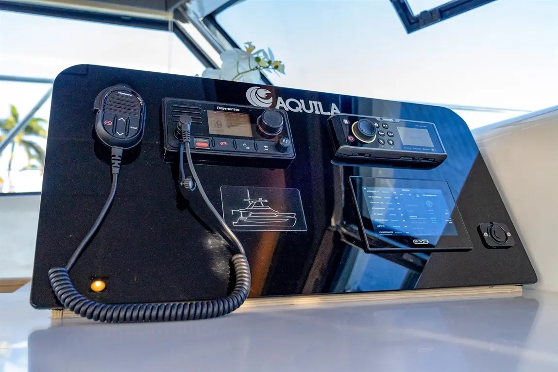 Black control panel labelled 'AQUILA' with Raymarine radio and various monitoring displays. Includes marine communication tools.
